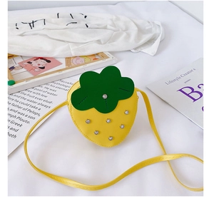 Close-up of yellow strawberry bag with green leaf detail and silver rivets on white fabric
