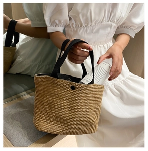 Detail view of natural handwoven straw tote with black handles and metal snap closure