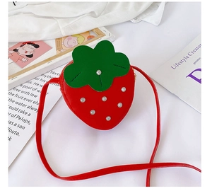Detail of red strawberry-shaped girl's crossbody bag with green leaf flap and metal studs