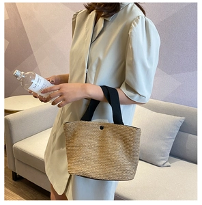 Detail of woven straw tote bag with black canvas straps and magnetic button closure
