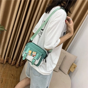 Détail d'un sac bandoulière en toile vert et beige avec badges cartoon sur un mannequin
