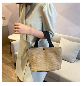 Detail of woven straw handbag with black fabric handles and a round magnetic snap closure