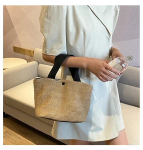 Detail of straw woven tote bag featuring black woven handles and a round button closure