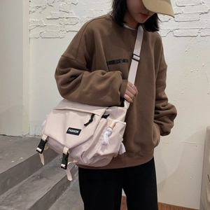 Detail of beige messenger bag featuring fashion tag, tassel charm, and buckle closure