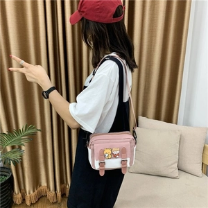Détail du sac bandoulière en toile rose et blanc avec patchs de dessin animé et sangle