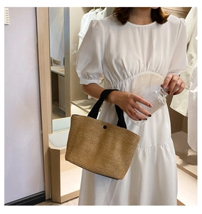 Detail of woven straw tote bag with black handles and a rustic texture for beach vacations