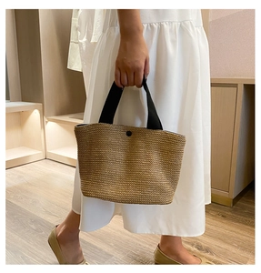 Detail of straw woven tote bag featuring natural texture and black canvas handles