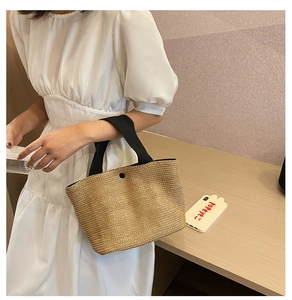 Detail of hand-woven straw beach bag with black wide straps and magnetic snap closure