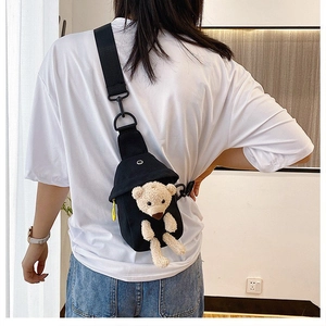 Detail of black canvas crossbody bag featuring a plush bear and yellow zipper accents
