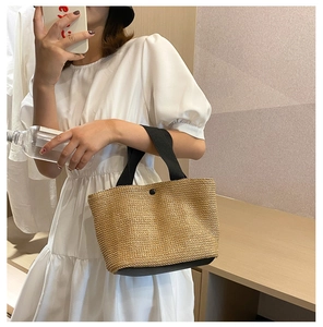 Detail of woven straw tote bag with black canvas handles and metal snap button closure