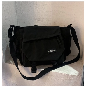 Detail view of large black messenger bag featuring buckle straps and fashion logo patch