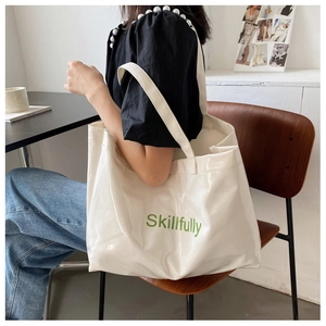 Détail d'un cabas blanc brillant avec texte vert Skillfully dans une scène de mode