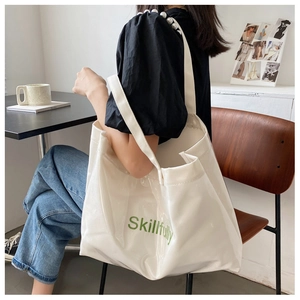 Détail d'un grand sac fourre-tout blanc avec texte vert montrant le style porté épaule