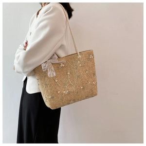 Détail du sac en paille avec broderie florale rose et nœud en dentelle blanche déco