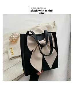 Detail of elegant black tote bag featuring a large cream bow on white tweed backdrop