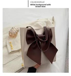 Detail of white tote bag featuring a large coffee-colored silk bow and gold hardware