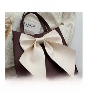 Detailed top view of a burgundy tote bag with a large cream bow and textured leather