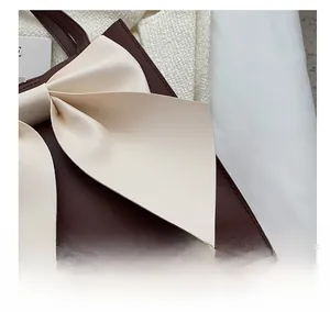 Detail showing high-precision stitching on a dark brown leather bag with cream bow