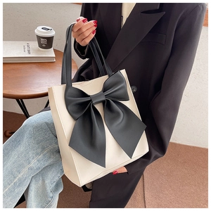Detail showing elegant off-white tote bag with a large decorative black bow and handles