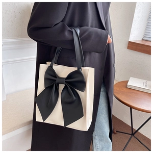 Detail of elegant cream tote bag with large black bow accent and long shoulder straps
