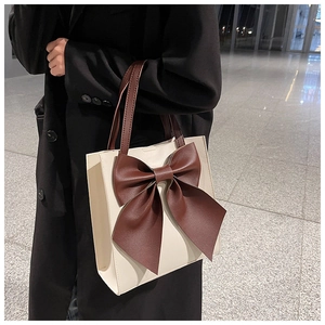 Detail of a chic tote bag featuring a large contrast bow and cream-brown leather stitching