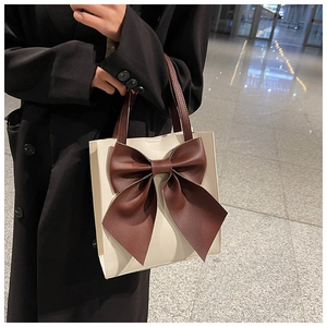 Detail of a square tote bag featuring a large decorative bow and brown leather handles