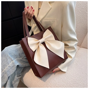 Detail view of a brown leather tote bag with a large cream bow held by a model