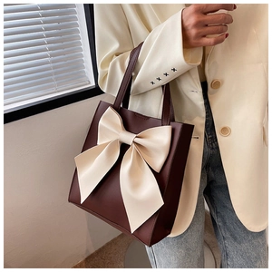 Detail of a brown tote bag with a large cream bow accent worn by a model in a beige blazer