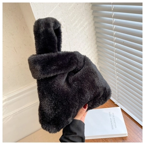 Detail of a plush black faux fur handbag with a unique knotted handle on a wooden desk