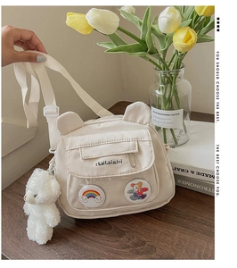 Close-up of beige nylon shoulder bag featuring cute bear badges and plush animal charm