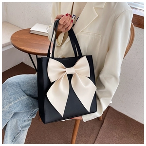 Detail of a black leather tote bag with a large white bow held by a model in a cafe