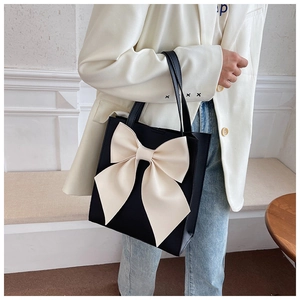 Close-up of stylish black tote bag with a large cream bow detail on minimalist background