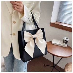 Detail of a black tote bag with a large beige bow shown in a lifestyle setting