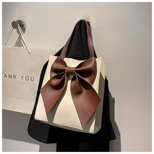 Detailed shot of a cream tote bag with large brown leather bow hung on a black blazer
