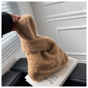 Detail of camel plush tote bag with knotted handle held over a minimalist book