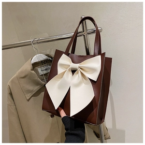 Detail of vintage brown tote bag with large cream bow and smooth leather texture