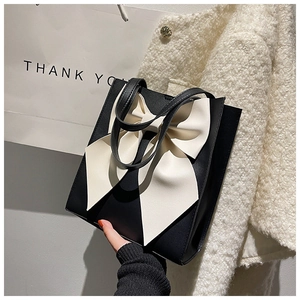 Detail of elegant black leather tote bag featuring a large cream white contrast bow accent