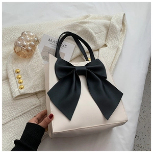 Detail of a chic cream handbag featuring a large black bow and vegan leather texture
