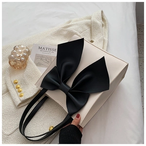Close-up of a large black silk bow detail on a stylish white leather tote bag