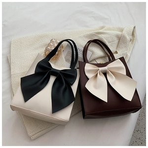 Detail of elegant tote bag featuring a large contrast satin bow and smooth faux leather