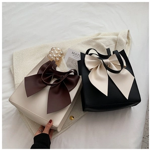 Detail of minimalist tote bags with large bow accents on beige tweed jacket