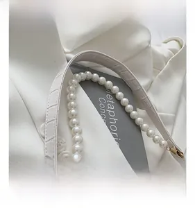 Detail of white crocodile texture leather strap with elegant pearl chain and gold hook