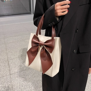 Minimalist white tote bag with large brown leather bow detail and shoulder strap