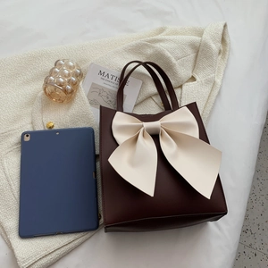Vintage dark brown tote bag with a large cream bow detail on a white textured backdrop