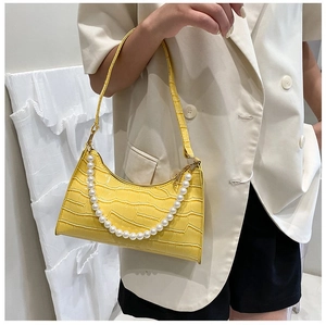Close-up of yellow crocodile texture baguette bag with large pearl chain detail