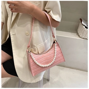 Detail of pink crocodile embossed handbag featuring a stylish white faux pearl decorative chain