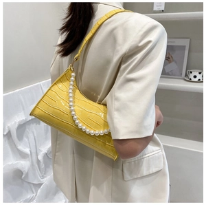 Detail of yellow crocodile embossed shoulder bag with elegant white pearl decorative chain
