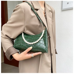 Close-up of green crocodile pattern handbag featuring decorative pearl handle and strap