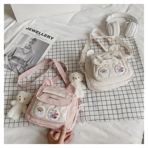 Detail of cute bear-eared nylon crossbody bags in pink and cream with rainbow badges