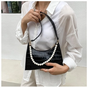 Detail of black crocodile texture underarm bag with white pearl chain and strap